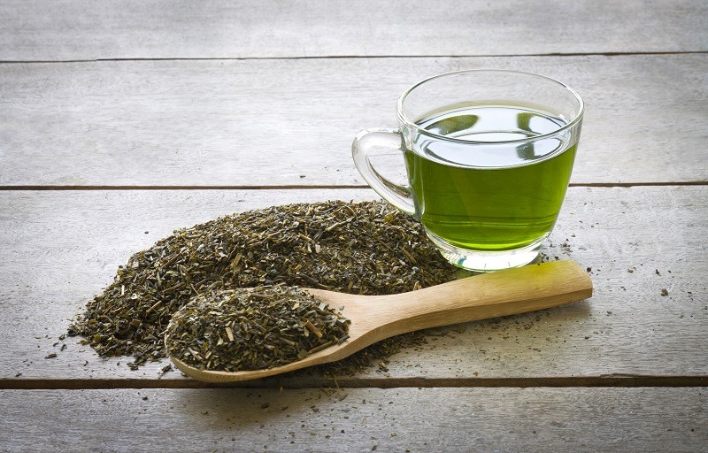 Tasse de thé vert et cuillère de feuilles de thé vert séchées sur fond en bois.