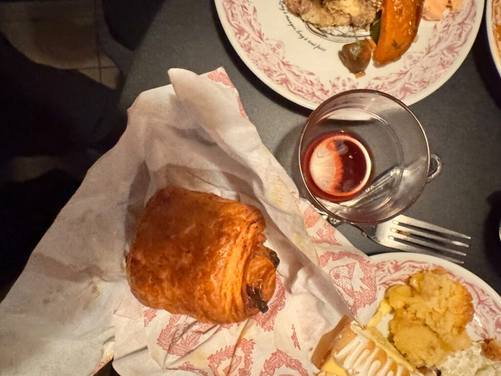 Viennoiserie (pain au chocolat) posée sur un papier kraft et un petit verre de jus de fruits rouge, lors du brunch au Mama Shelter Paris East.
