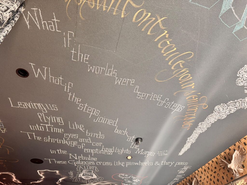 Plafond gris foncé du restaurant Mama Shelter Paris East orné d'inscriptions à la craie blanche et dorée. On peut y lire des phrases poétiques comme "What if the worlds were a series of steps" et "Leaving us flying like birds into Time", accompagnées de dessins et d'une grande inscription dorée.