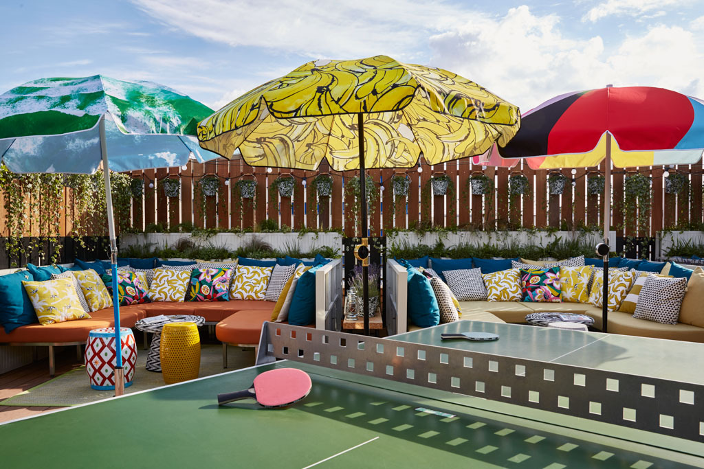 Vue d'ensemble de la terrasse ensoleillée du Mama Shelter Paris East avec ses tables multicolores, aménagée pour le brunch d'été du dimanche.