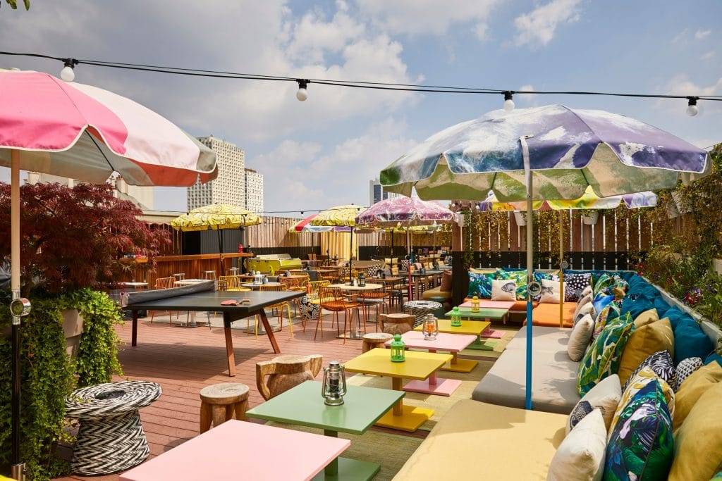 Terrasse extérieure du Mama Shelter Paris East avec une table de ping-pong, des canapés colorés et de grands parasols, lieu du brunch d'été le dimanche.